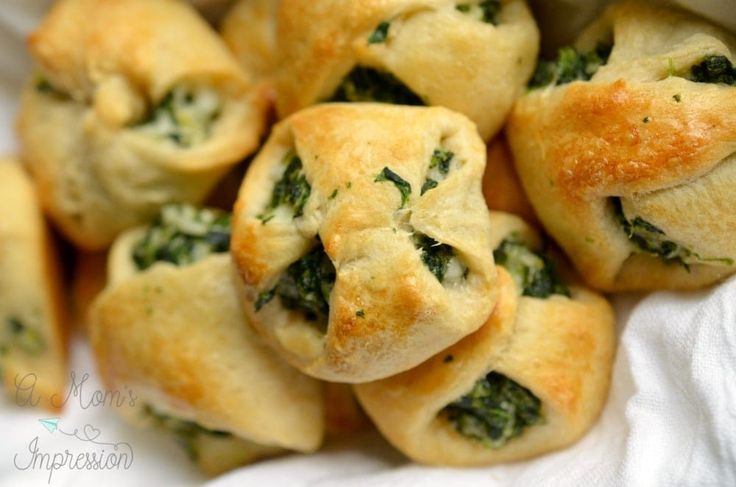 small pastries with spinach and cheese are on a white cloth in a basket