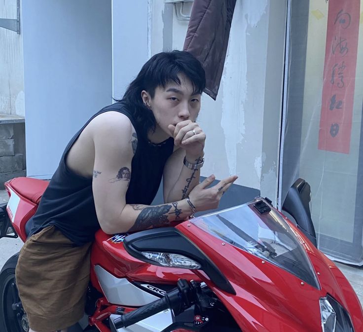 a man with tattoos on his arm leaning on a red motorcycle