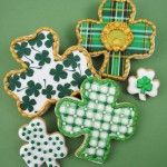 four decorated shamrock cookies sitting on top of a green tableclothed surface with gold trimmings