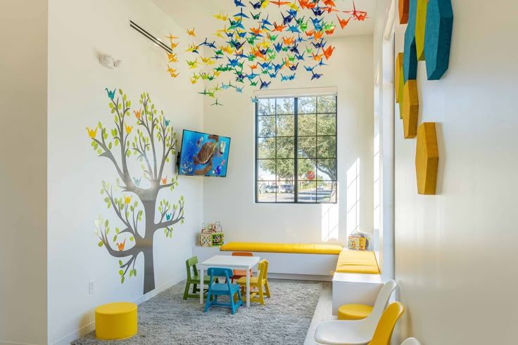 the children's room is decorated in bright colors and has a tree painted on the wall