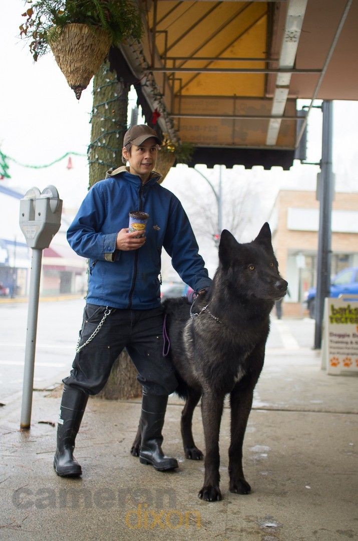 a man standing next to a large black dog on a leash and holding a drink