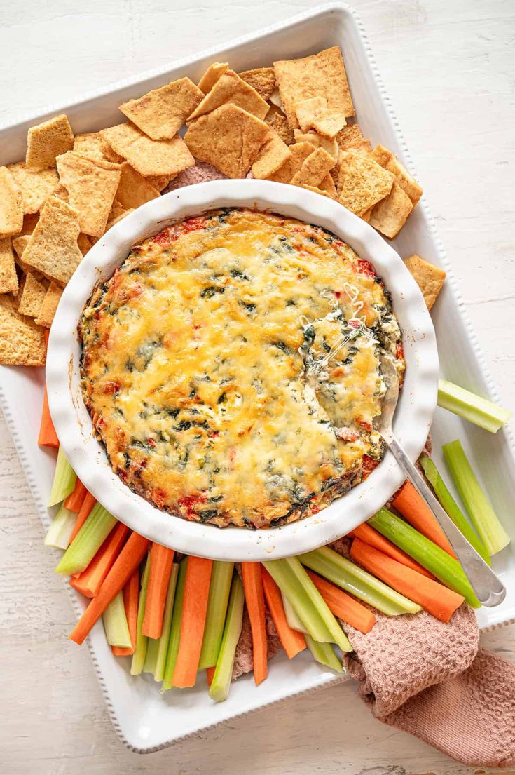 a white plate topped with dip surrounded by crackers and veggies