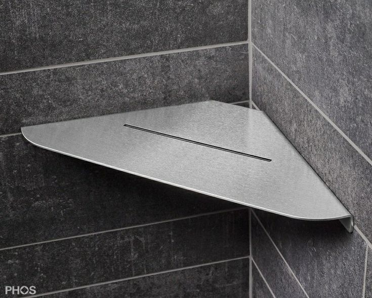 the corner of a shower with a metal shelf on it's side in a tiled wall