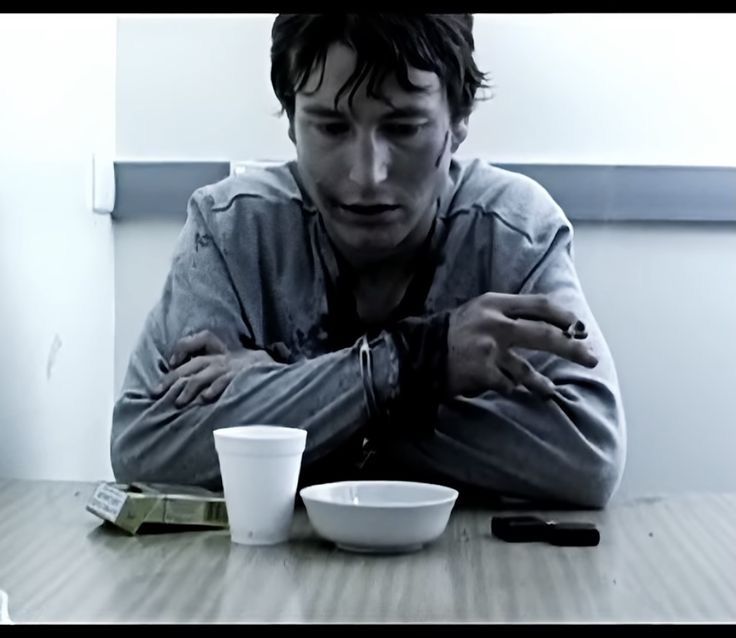 a man sitting at a table with his hands on his chest and looking down while eating from a white bowl