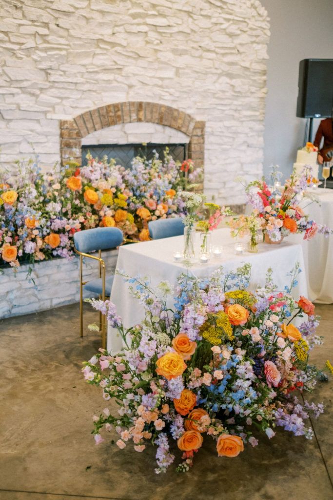 an arrangement of flowers on a table in front of a fire place with chairs around it