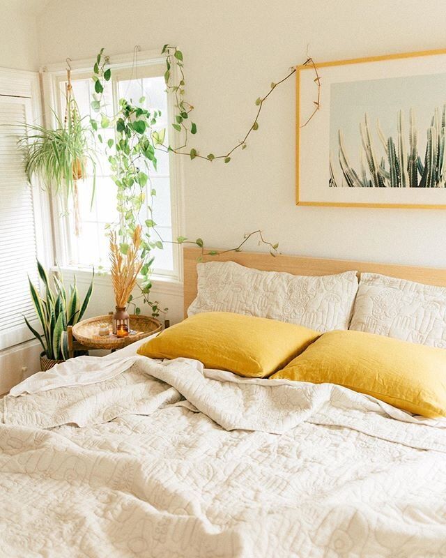 a bed with white sheets and yellow pillows in a bedroom next to a potted plant