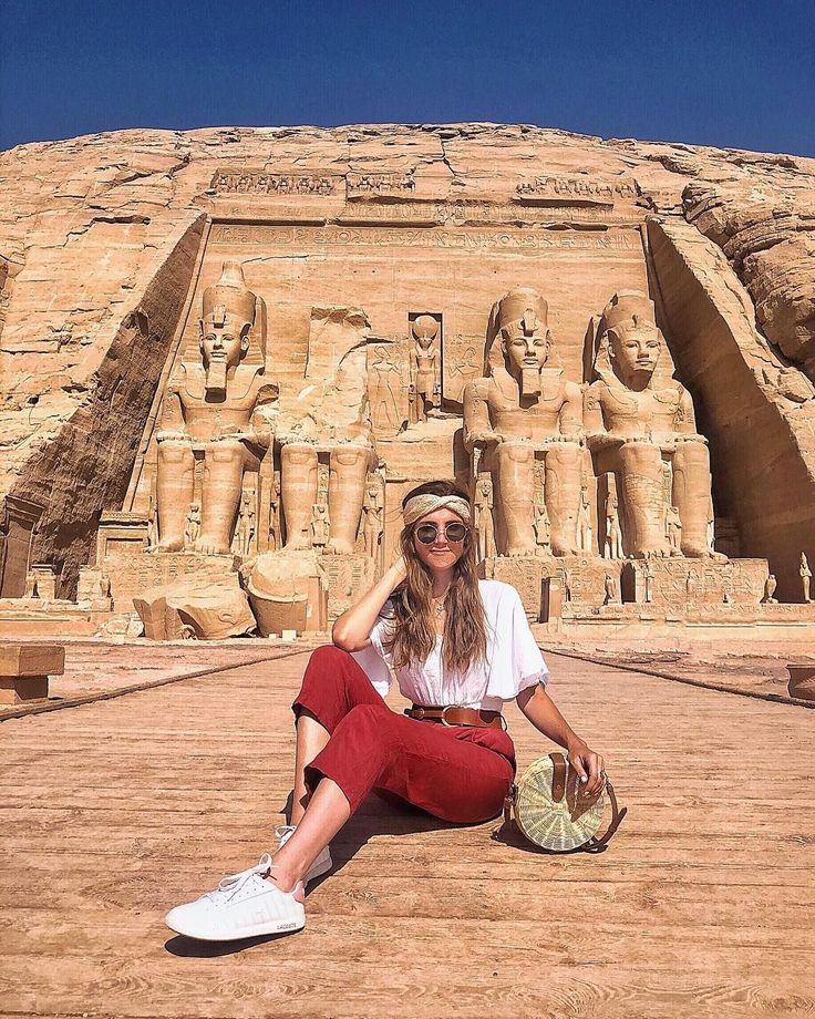 a woman is sitting on the ground in front of an egyptian temple with her hat and sunglasses on