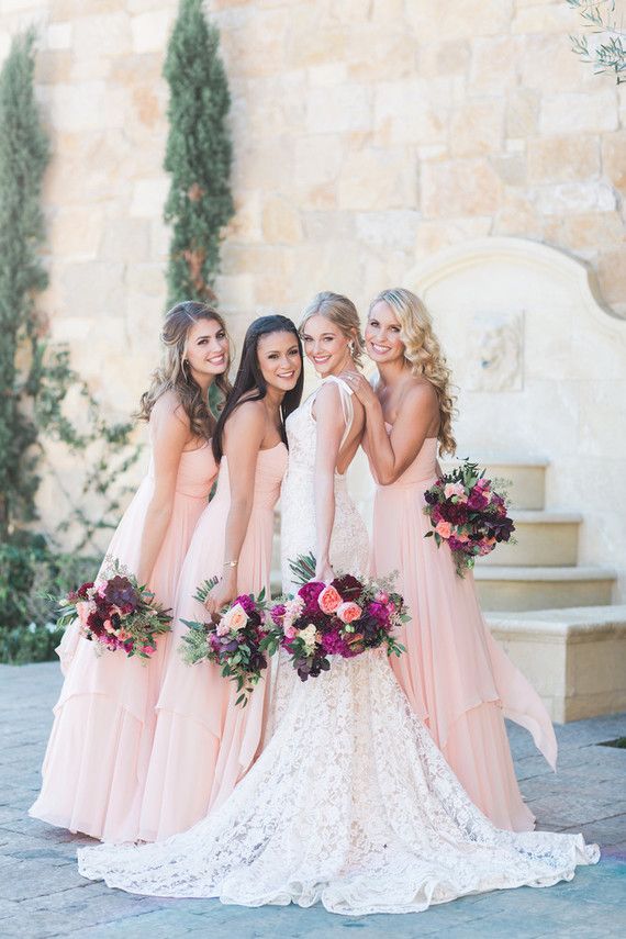 a group of women standing next to each other in front of a stone wall with flowers