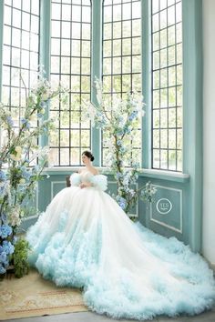 a woman in a blue dress sitting on a window sill with flowers and greenery