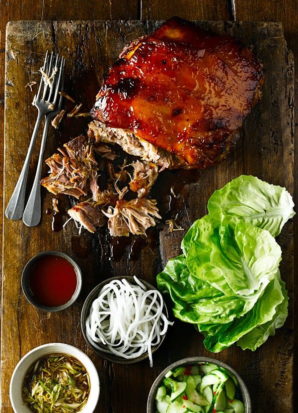 a wooden cutting board topped with meat and veggies next to dipping sauces