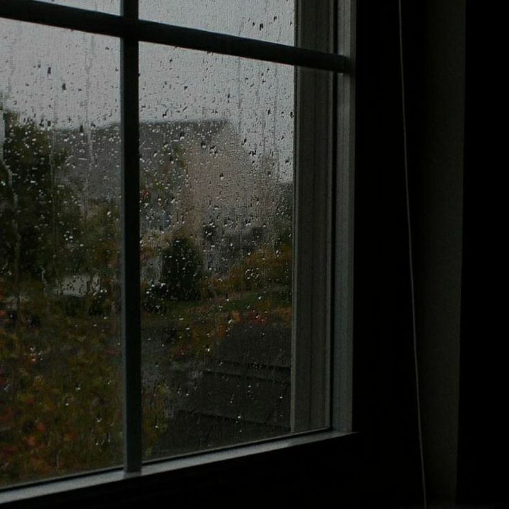 a window with rain drops on it in front of a house and trees outside the window