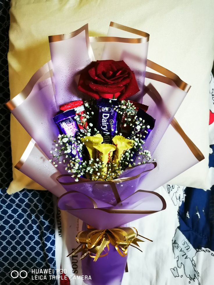 a bouquet of chocolates and candy wrapped in purple paper with a rose on top