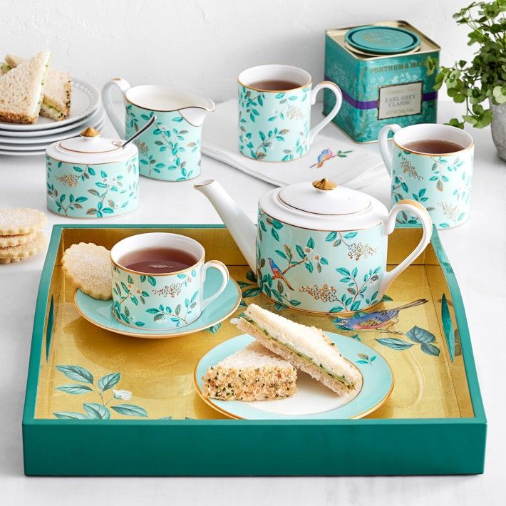 a tray with tea cups, sandwiches and cookies on it next to other items such as crackers