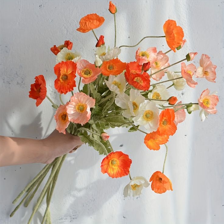 a person holding a bouquet of flowers on a white tablecloth with orange and white flowers in it