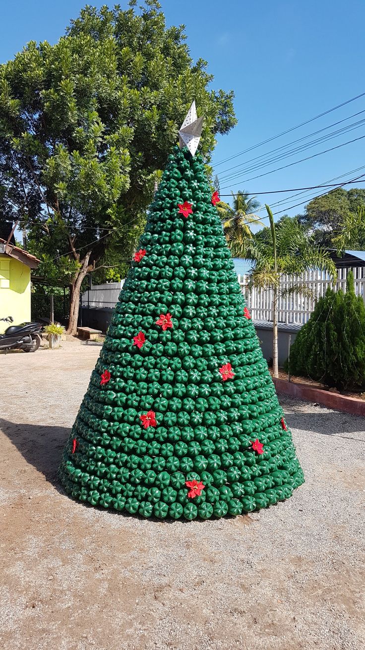 a large green christmas tree made out of plastic bottles in the middle of a driveway