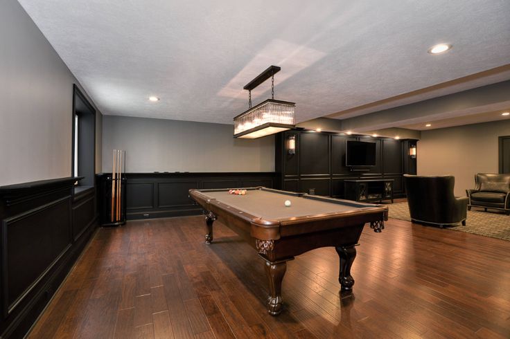 a pool table in the middle of a room with dark wood floors and black walls