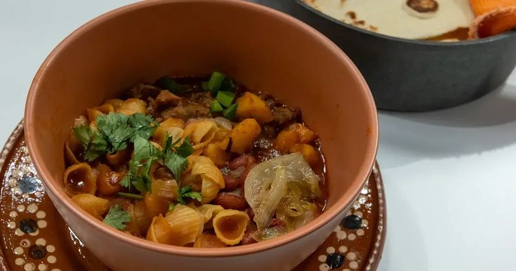 a bowl filled with pasta and vegetables on top of a plate next to another bowl