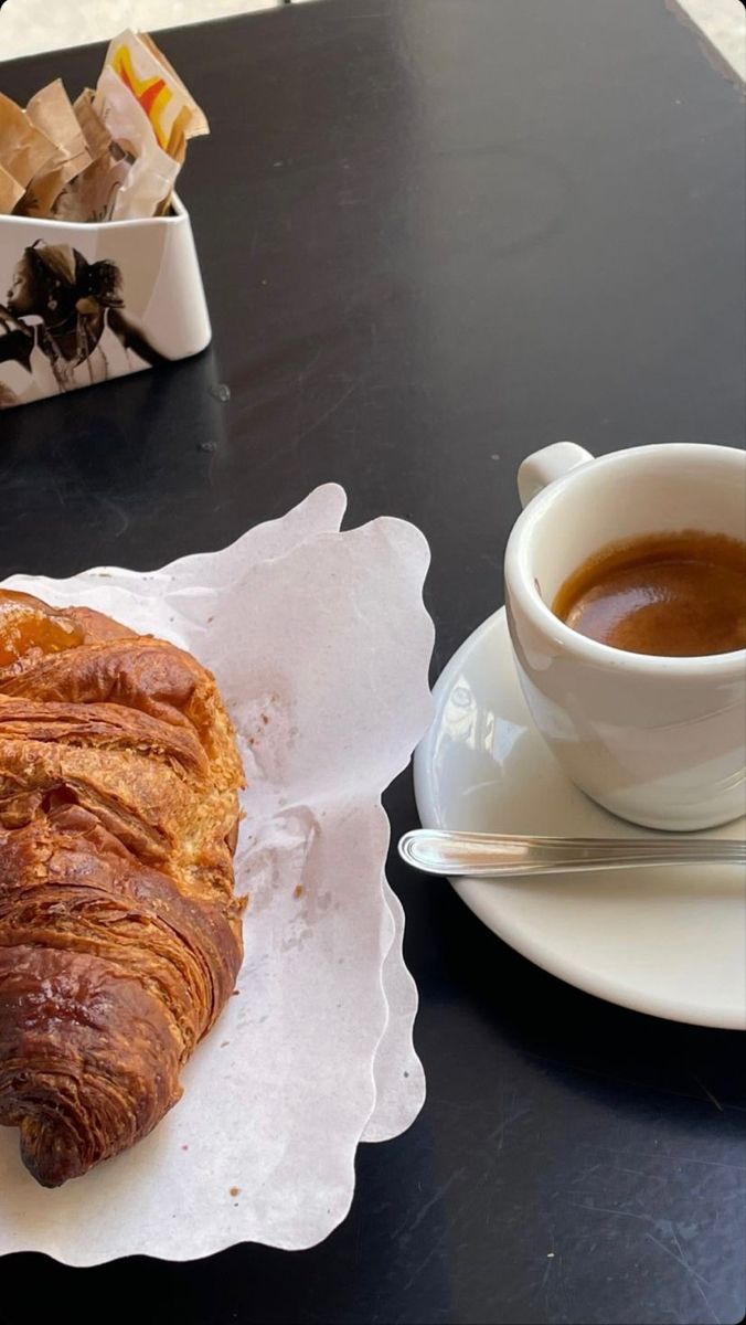 a croissant sitting on top of a white plate next to a cup of coffee