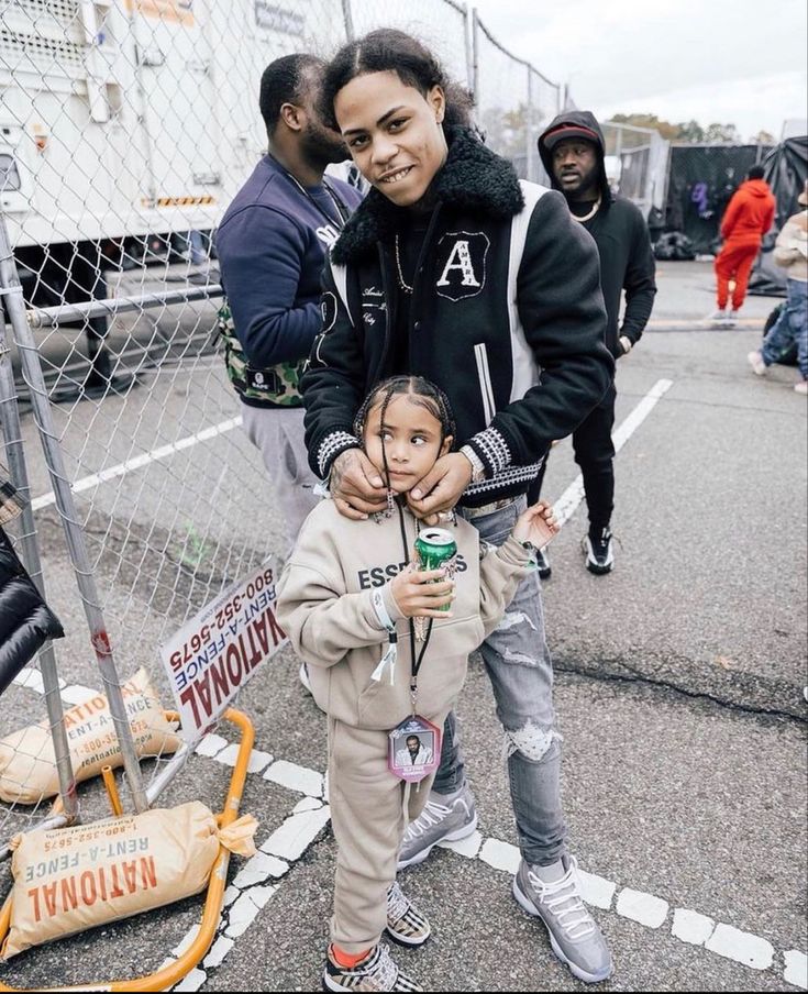 a woman and child standing in front of a chain link fence at an outdoor event