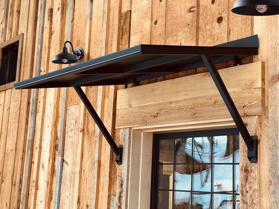 a black metal shelf on the side of a wooden building with a window and light fixture