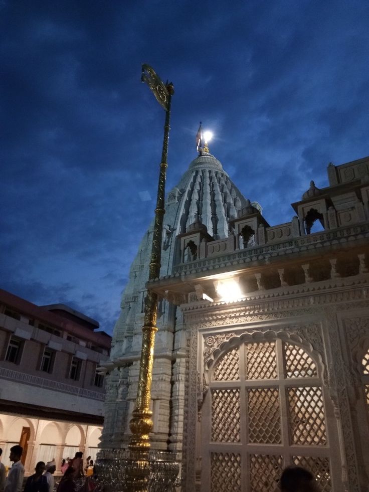 people are walking around in front of an ornate building at night with the lights on