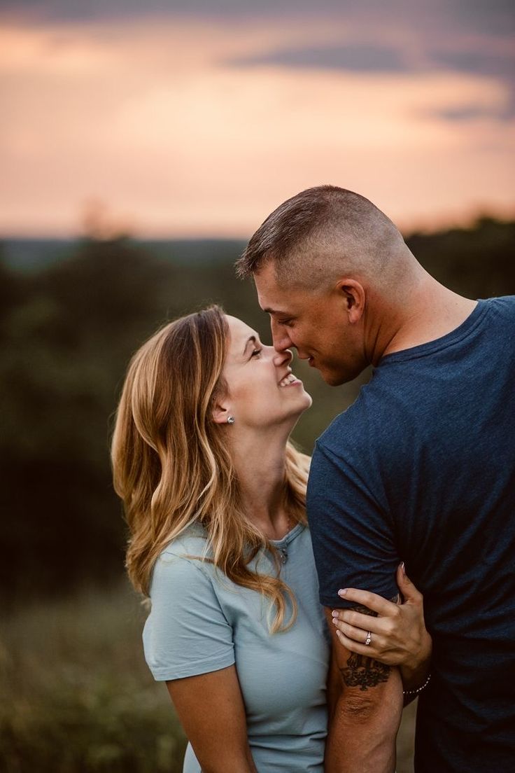 a man and woman standing next to each other in front of the sky at sunset