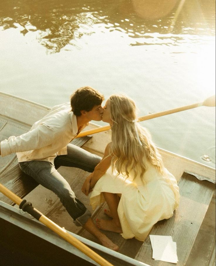 a man and woman sitting in a row boat on the water kissing while holding onto each other's tails