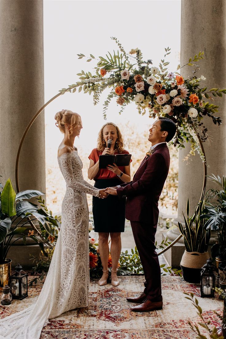 a bride and groom exchanging vows in front of an arch with greenery on it