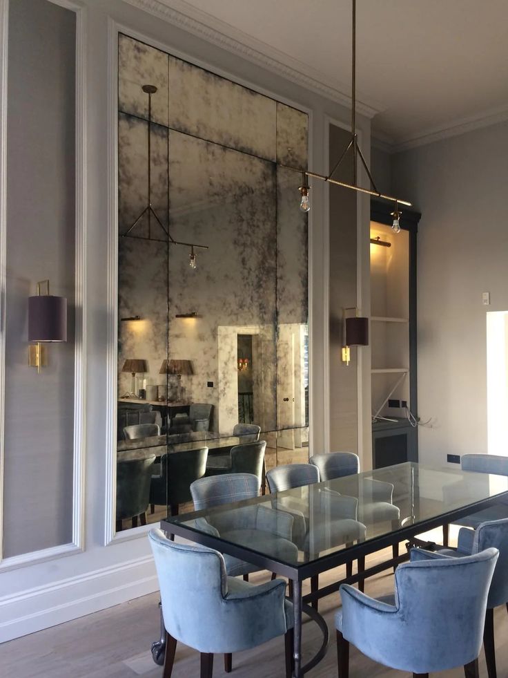 a glass dining table with blue chairs in front of a large mirror wall and floor to ceiling windows