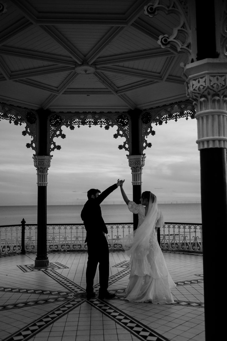 a bride and groom dance under an ornate gazebo at their wedding reception in front of the ocean