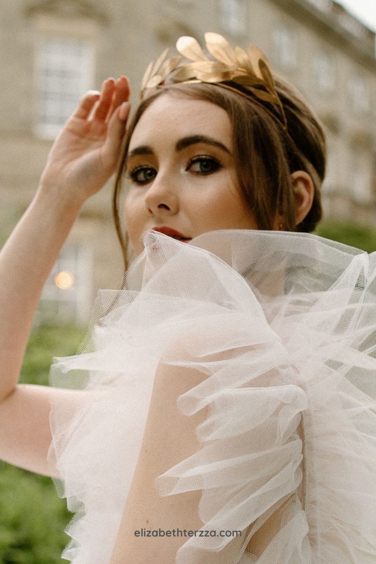 a woman wearing a white dress and a gold tiara is posing for the camera