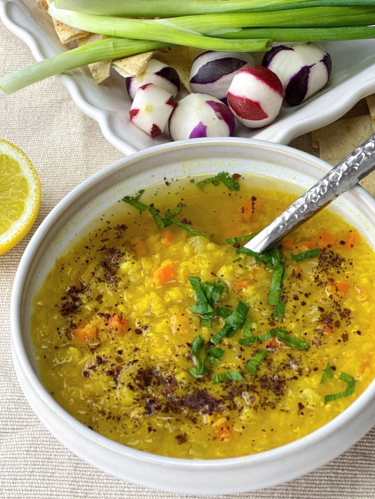 a bowl of soup with carrots, onions and celery on the side