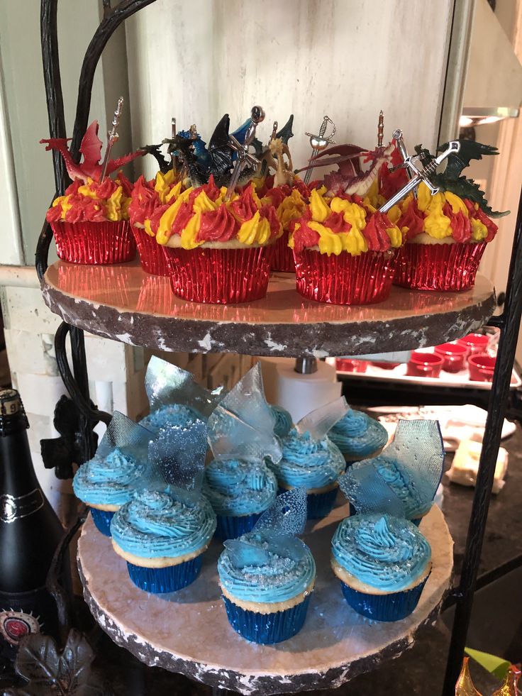 cupcakes and muffins are displayed on three tiered platter with red, yellow and blue frosting