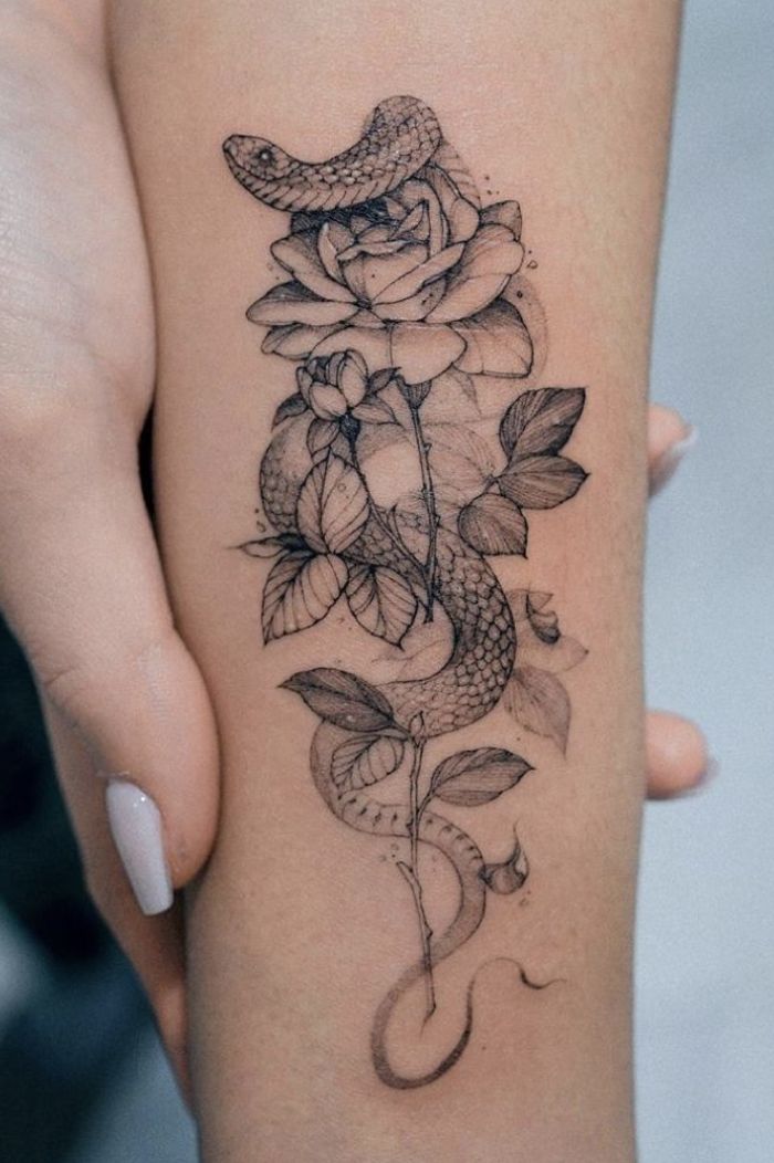 a woman's arm with a snake and rose tattoo on it, while she is holding