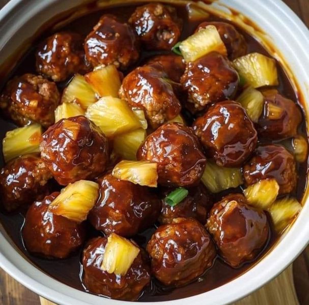 meatballs and pineapples are in a white bowl on a wooden table, ready to be eaten