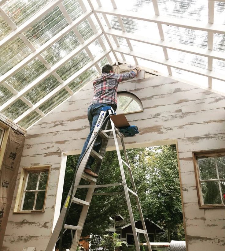 a man standing on top of a ladder in front of a house under construction with windows