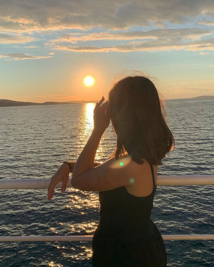 a woman standing on the deck of a boat looking out at the ocean as the sun sets