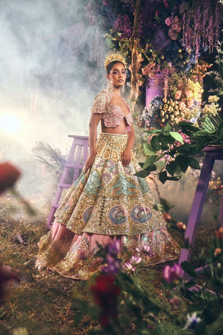 a woman wearing a gold and pink dress standing in front of a flower covered bench