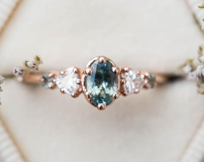 an engagement ring with blue and white stones on it's side, sitting on top of a cloth