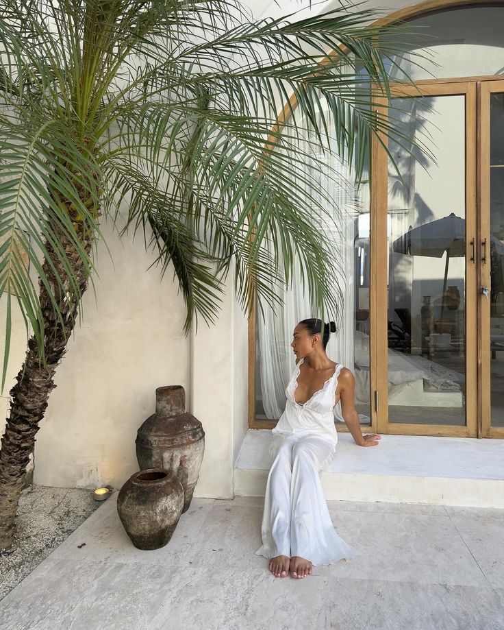 a woman sitting in front of a palm tree next to a large potted plant