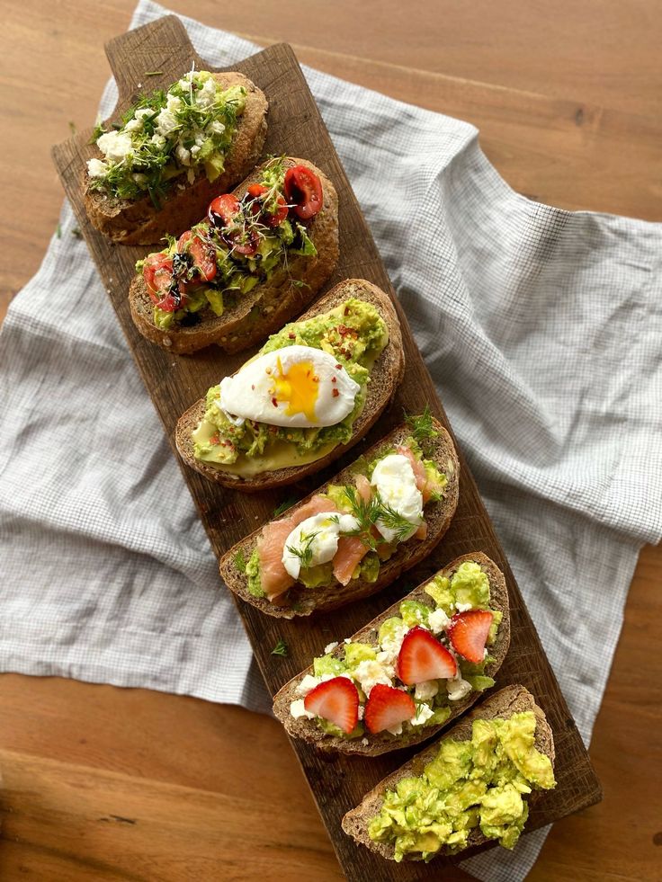 four open faced sandwiches with lettuce, tomato and an egg on them sitting on a cutting board