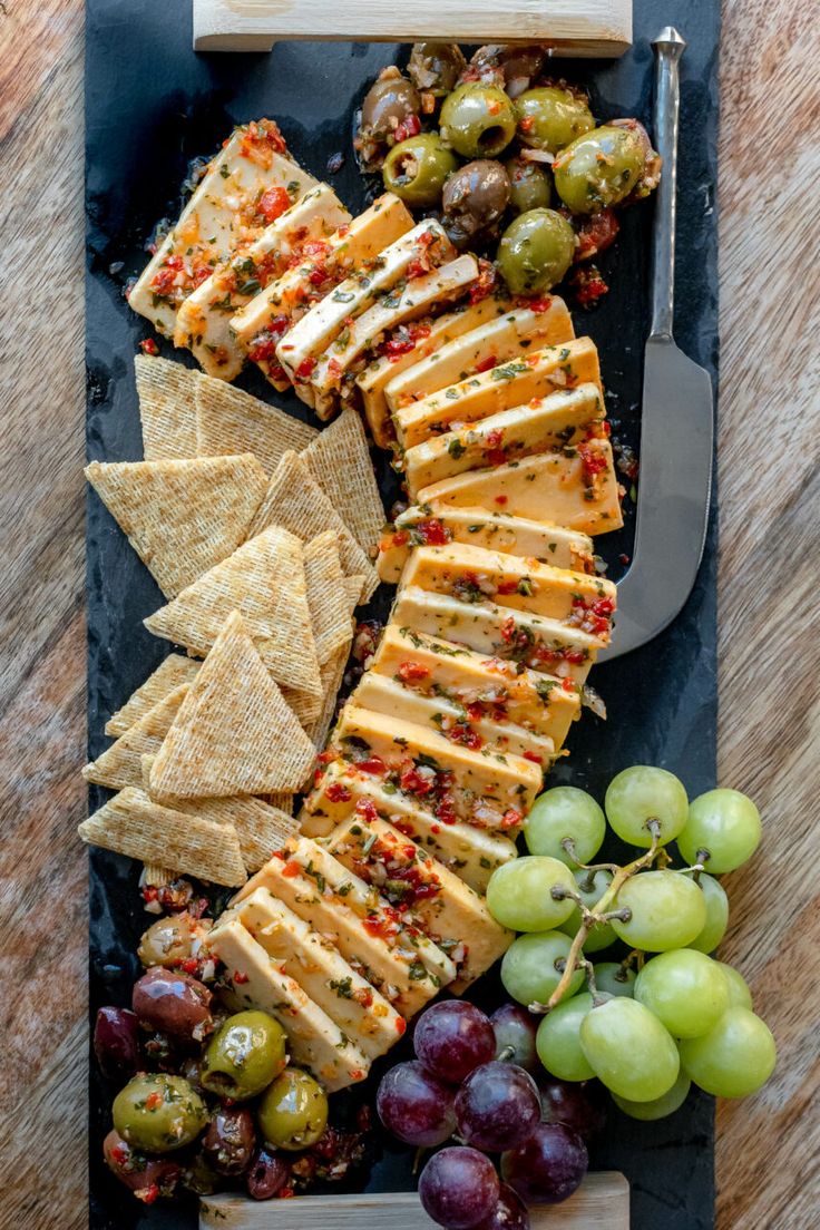 an assortment of cheeses, crackers and grapes on a slate platter