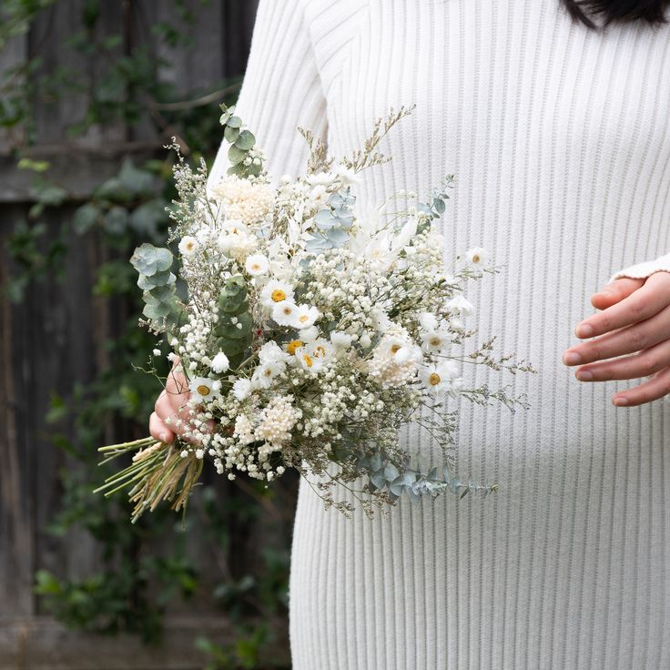 a woman holding a bouquet of white flowers in her left hand and wearing a sweater