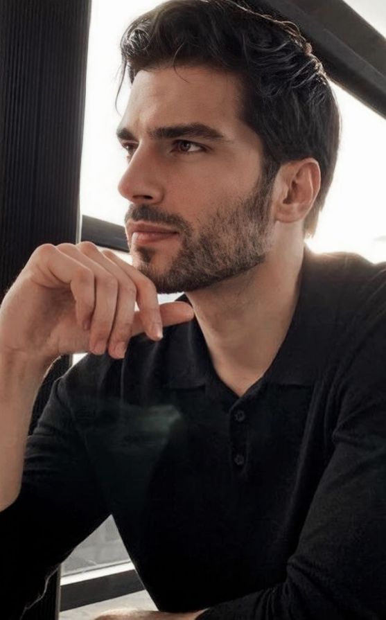 a man sitting at a table in front of a window with his hand on his chin