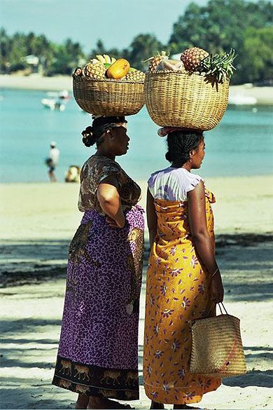 two women with baskets on their heads standing at the beach