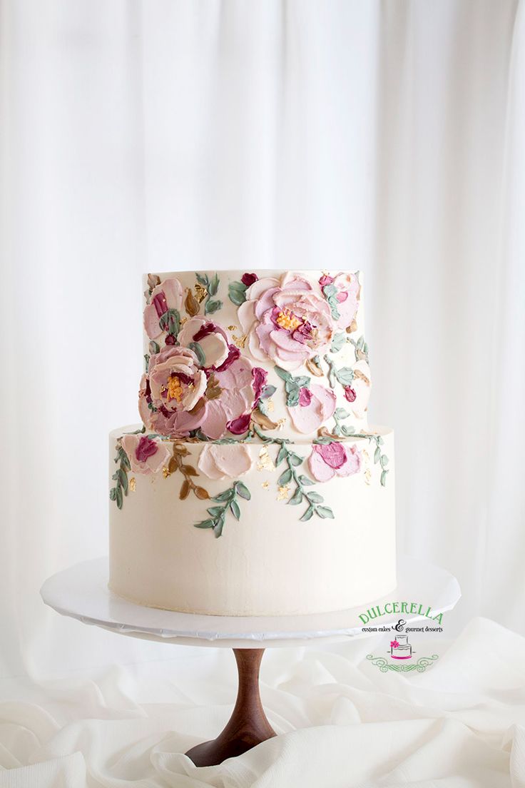 a three tiered cake with pink flowers on it sitting on top of a white table cloth