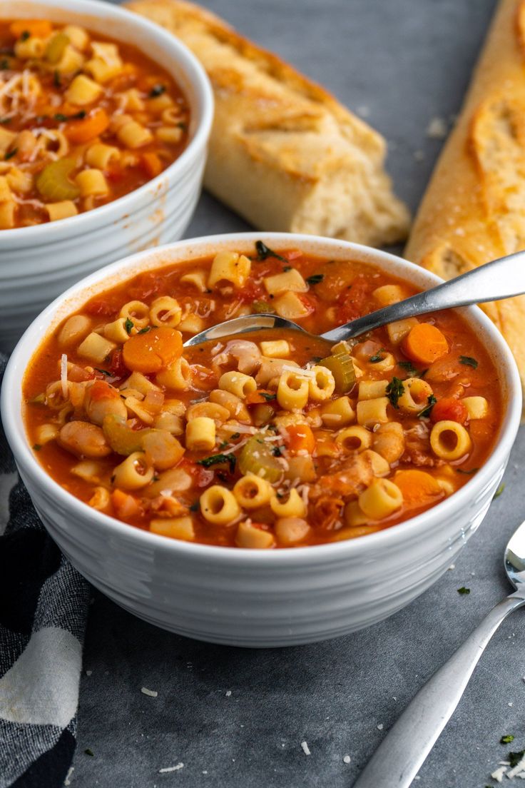 two bowls of pasta soup with bread on the side