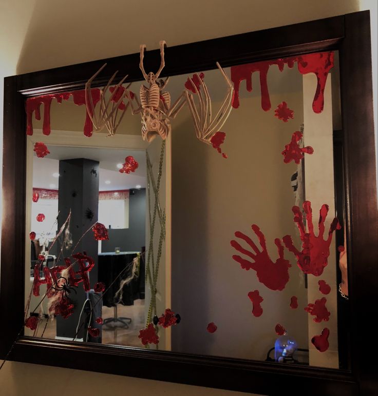 a mirror that has some red paint on it and a skeleton hanging from the frame