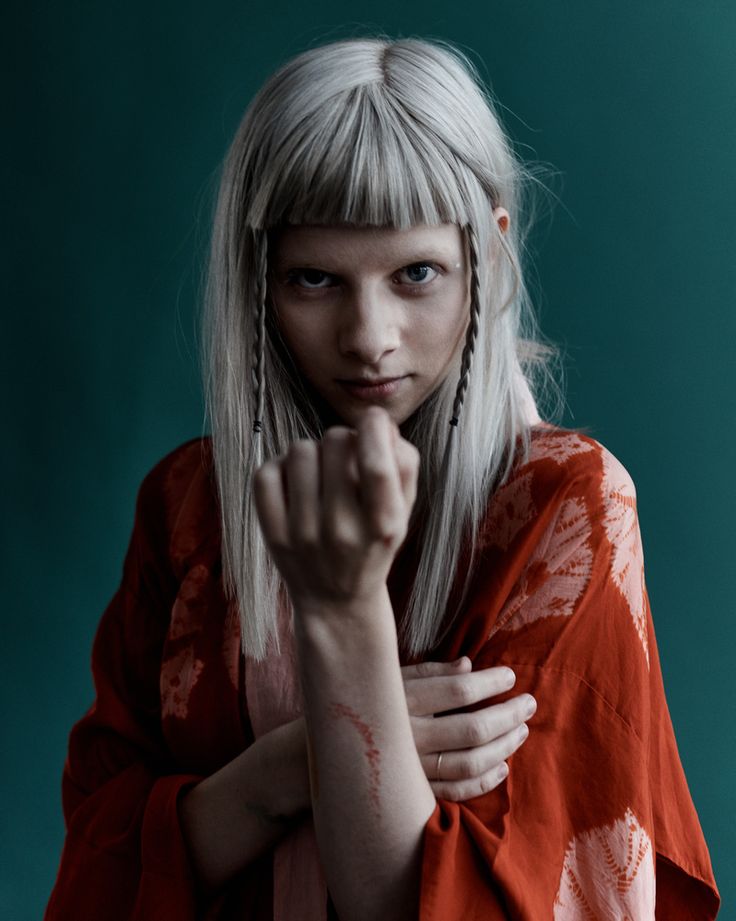 a woman with blonde hair wearing an orange shirt and holding her hand up to the camera