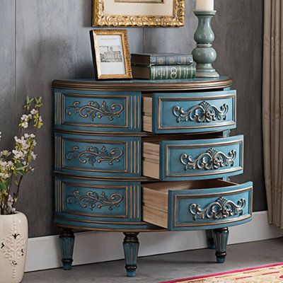 an ornate blue chest of drawers in front of a painting and vase with flowers on it